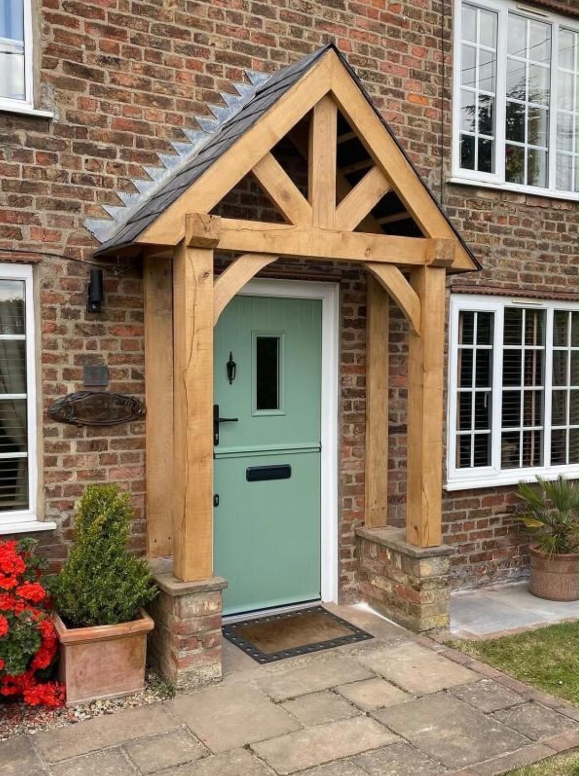 An oak-framed porch canopy with a green stable door on a period brick cottage.